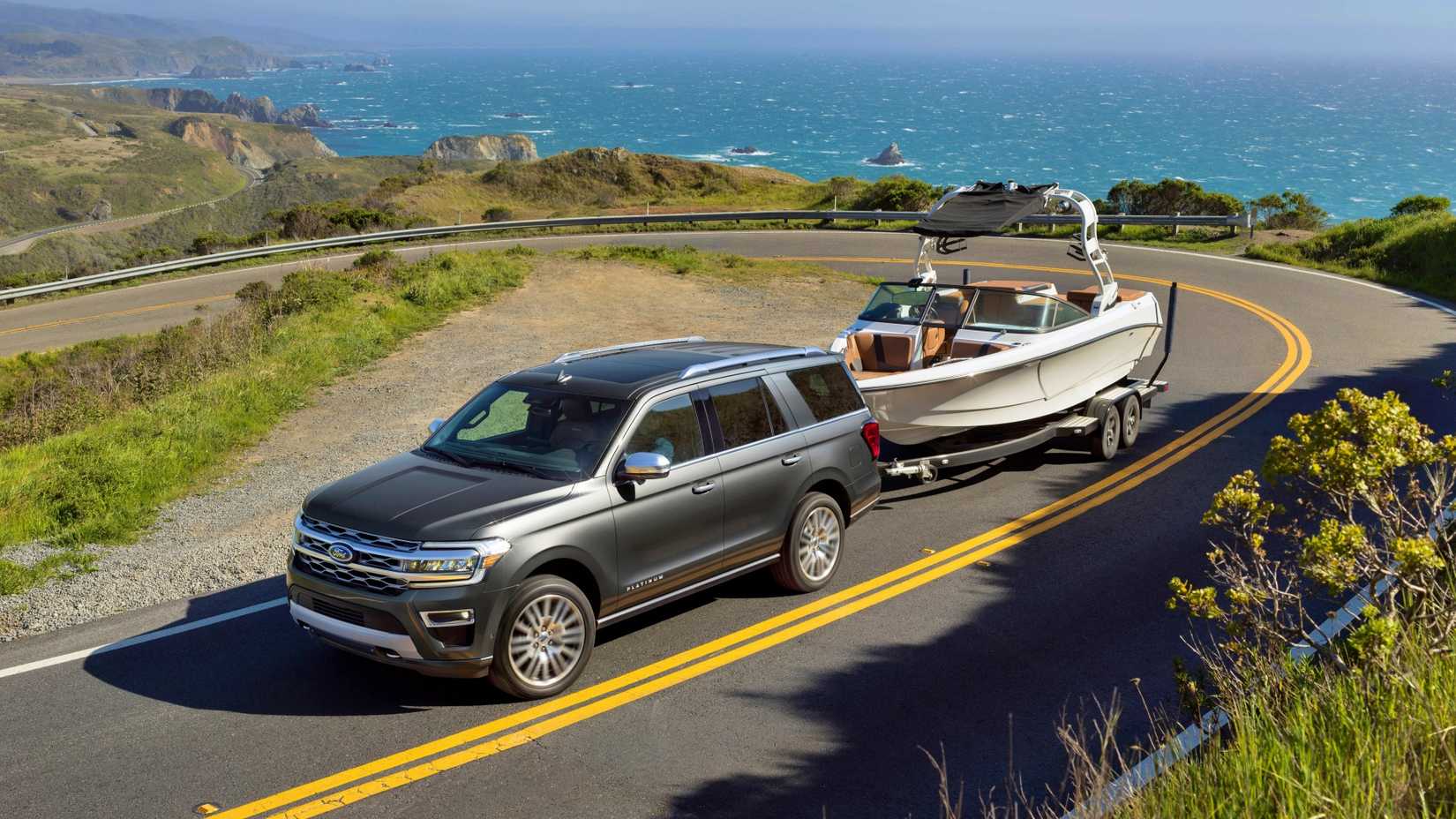 Uma cena de ação de um Ford Expedition Platinum 2022 rebocando um barco por uma estrada na montanha