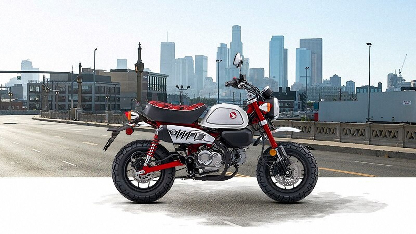 Red 2023 Honda Monkey static profile shot with city backdrop