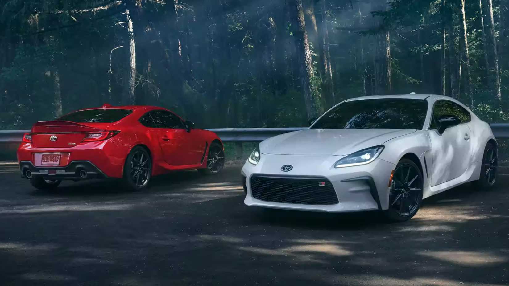 Red and white Toyota GR86 front and rear quarter view parked in front of trees