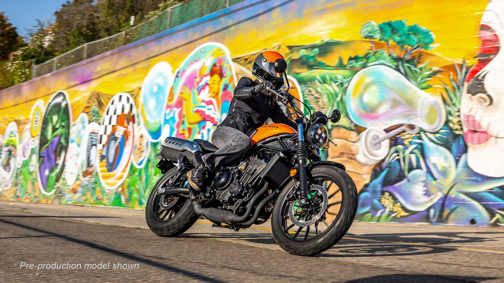 Orange 2023 Honda SCL500 cruising by a graffiti wall