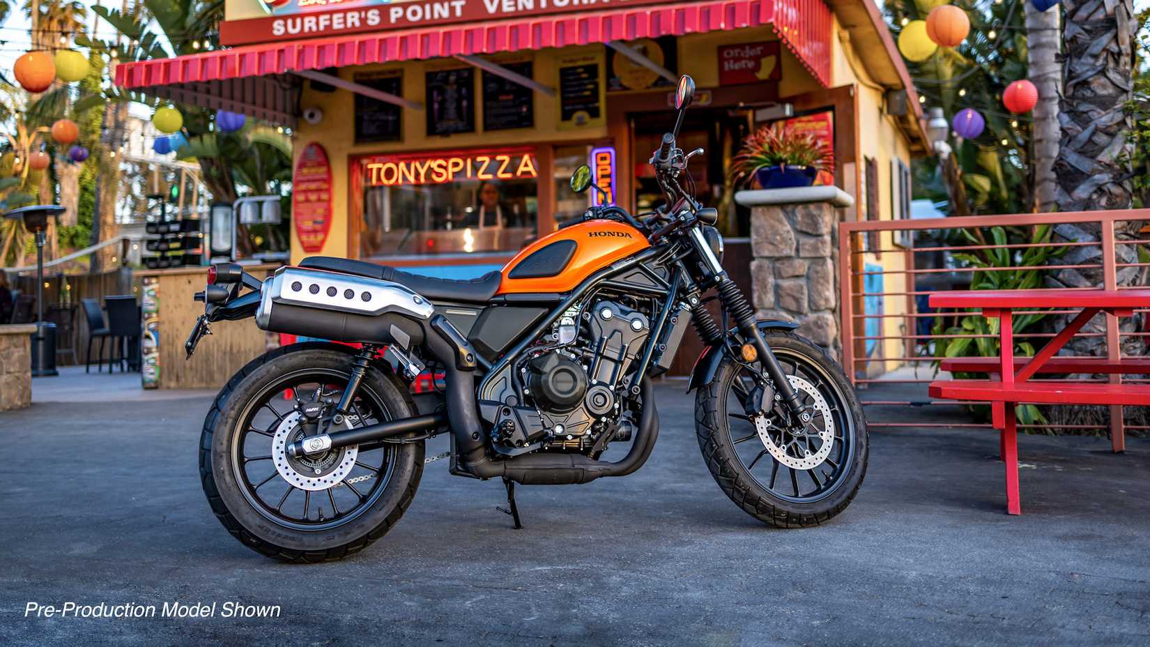 Orange 2023 Honda SCL500 parked outside a pizzeria