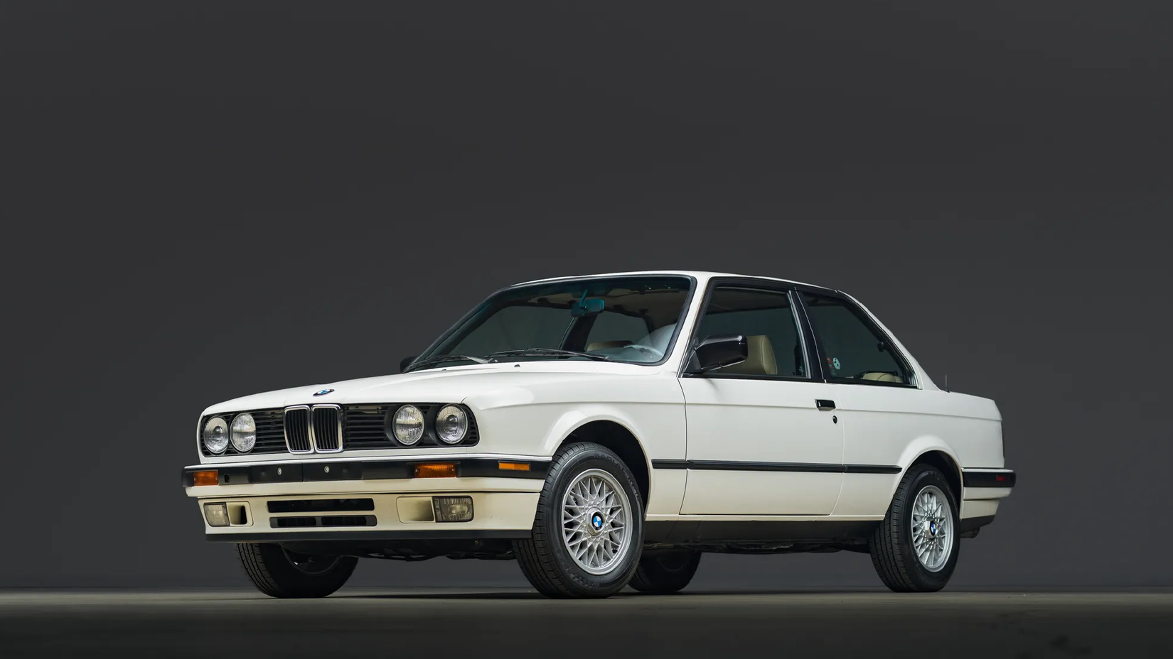 A white BMW 325i coupe (E30) in a studio