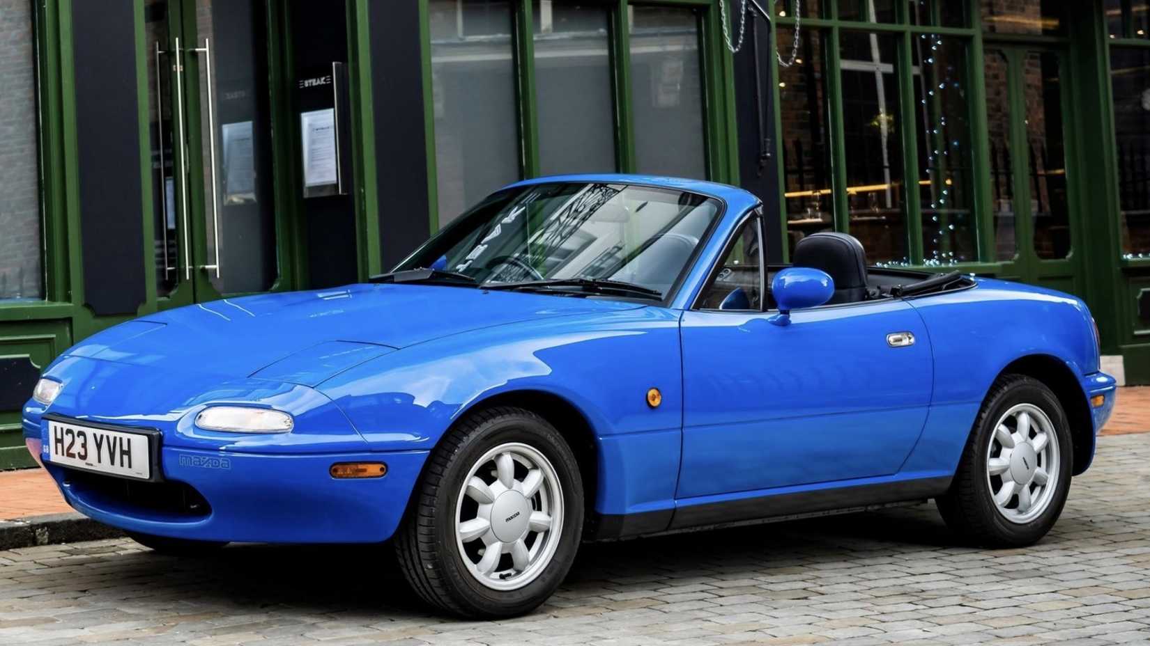 1990 Mazda Miata MX-5 in blue posing in front of building with convertible roof down