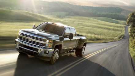 2015 Chevrolet Silverado HD em preto dirigindo em estrada secundária com campo e árvores ao fundo