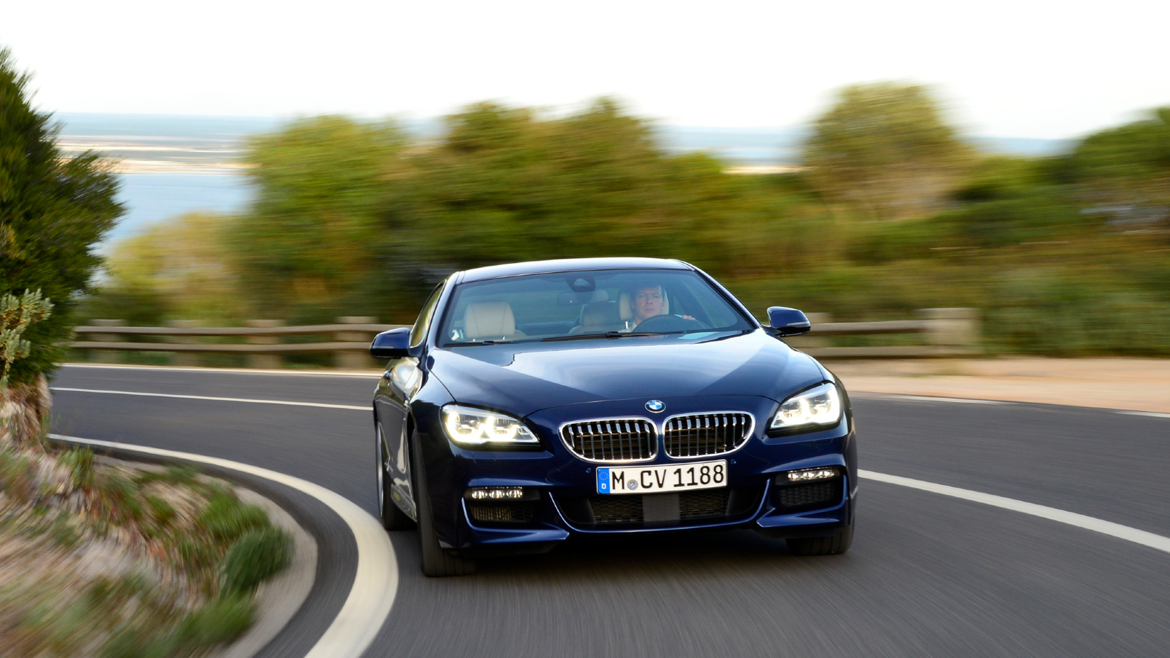 A Blue 2012 BMW 650i been driven on the road on a hill. 