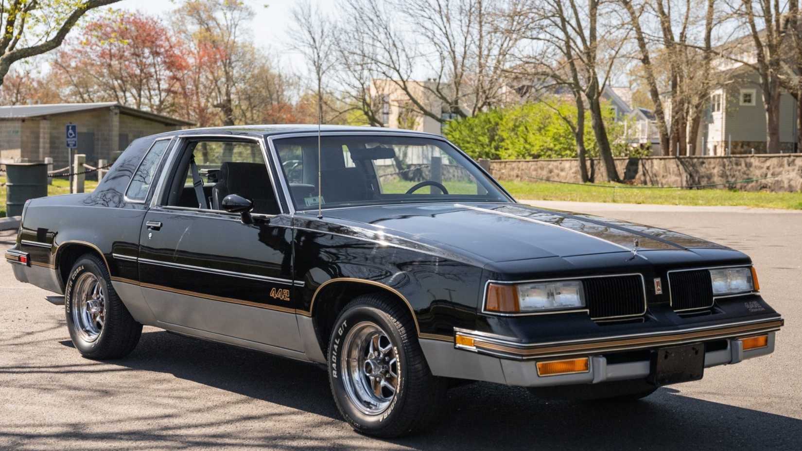 Oldsmobile 4-4-2 1987 em preto posando em uma rua suburbana