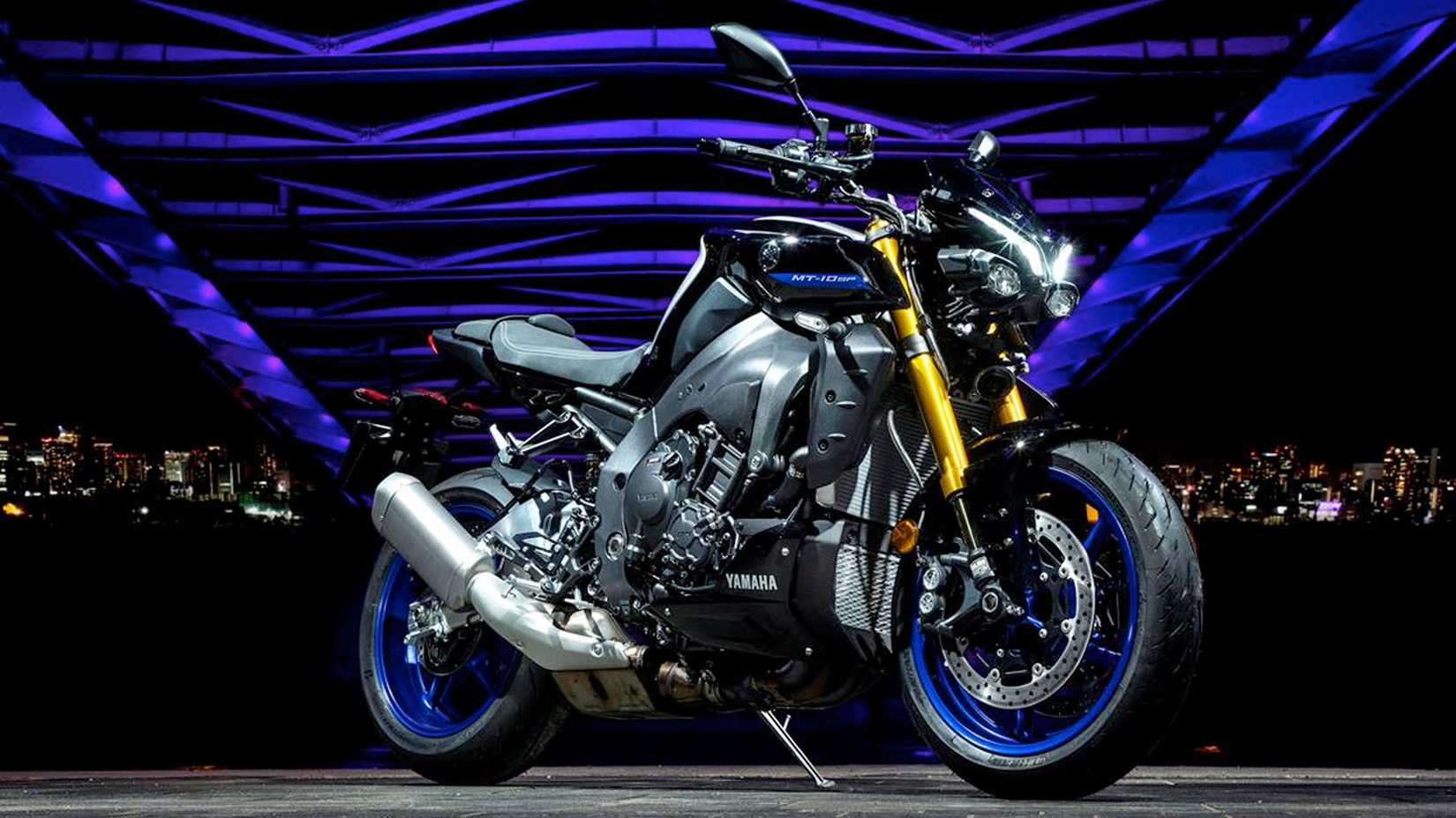 Photograph of a 2023 YAMAHA MT-10 parked under a lit up bridge at night with a city skline backdrop.