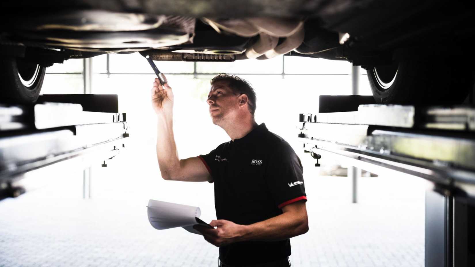 A Porsche Mechanic inspecting underneath a lifted car in a service center.