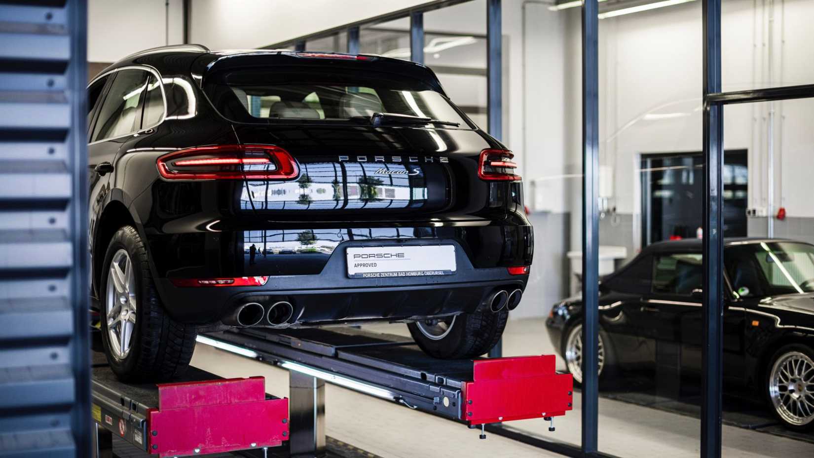 Rear shot of a 2021 Porsche Macan S lifted in a service center, with a Porsche Approved sign on the plates.