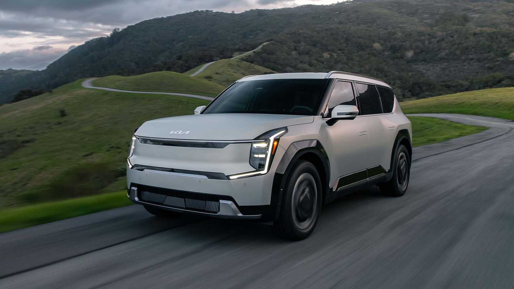 Front 3/4 view of a 2024 Kia EV Land AWD driving down winding road