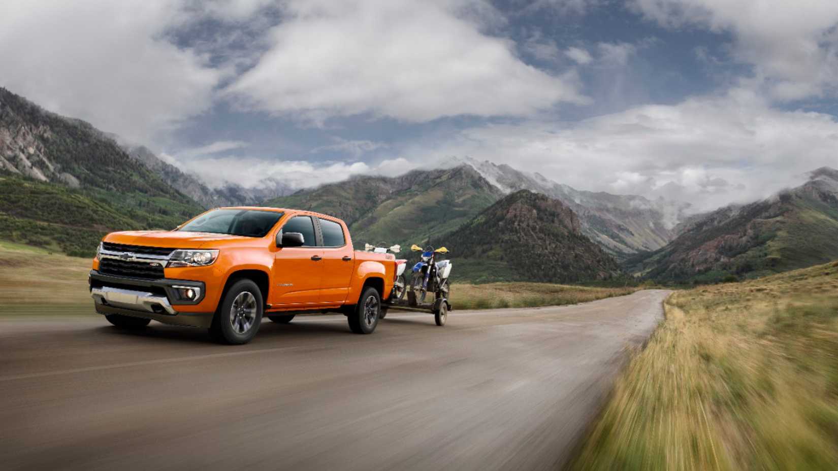 3/4 shot of 2021 Chevrolet Colorado in orange driving on mountain road, towing trailer with dirt bikes on
