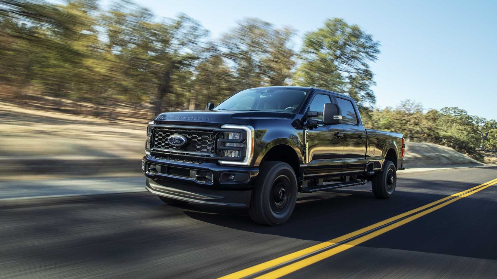 Foto frontal de ação 3/4 de um Ford Super Duty F-250 XL 2023 com o pacote de aparência STX dirigindo ao longo de uma estrada