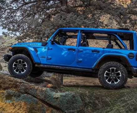 Perfil lateral de um Jee Wrangler 4xe 2024 azul com teto aberto estacionado no deserto