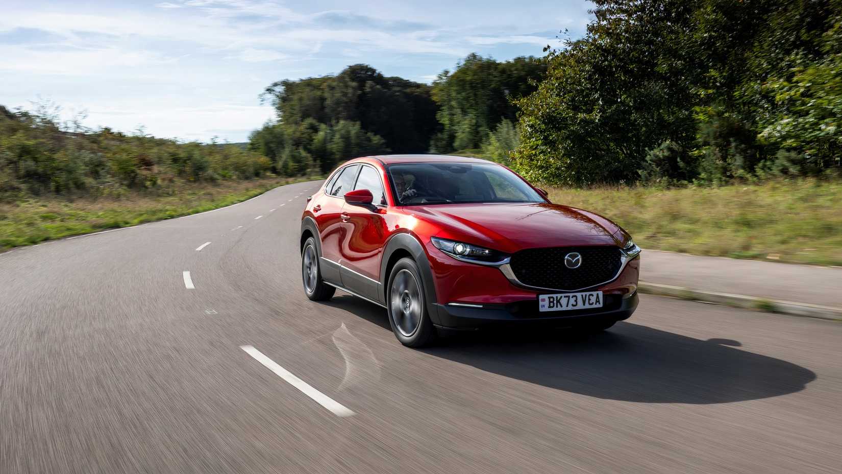 Foto frontal de um Mazda CX-30 2024 dirigindo em uma estrada sinuosa