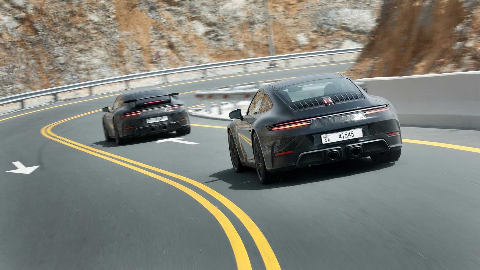 Two black Porsche 911 Hybrid prototypes driving down a highway