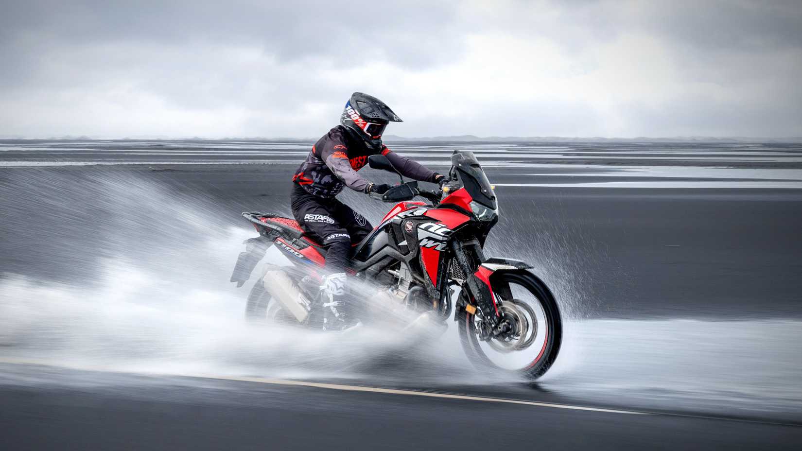 A dramatic shot of the Africa Twin blasting through a beach 
