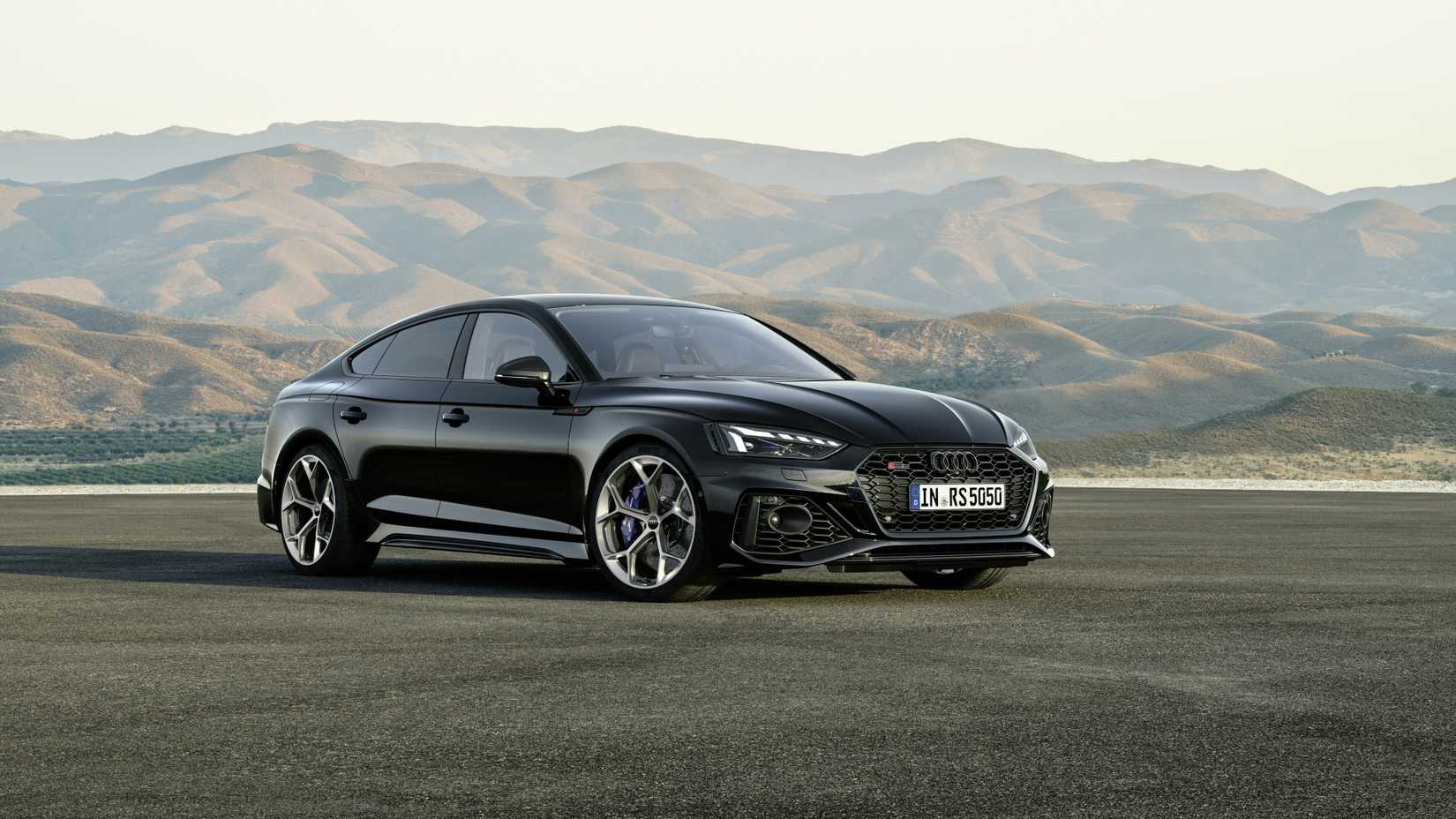 Foto frontal 3/4 de um Audi RS5 Sportback 2024 preto estacionado em frente a algumas montanhas
