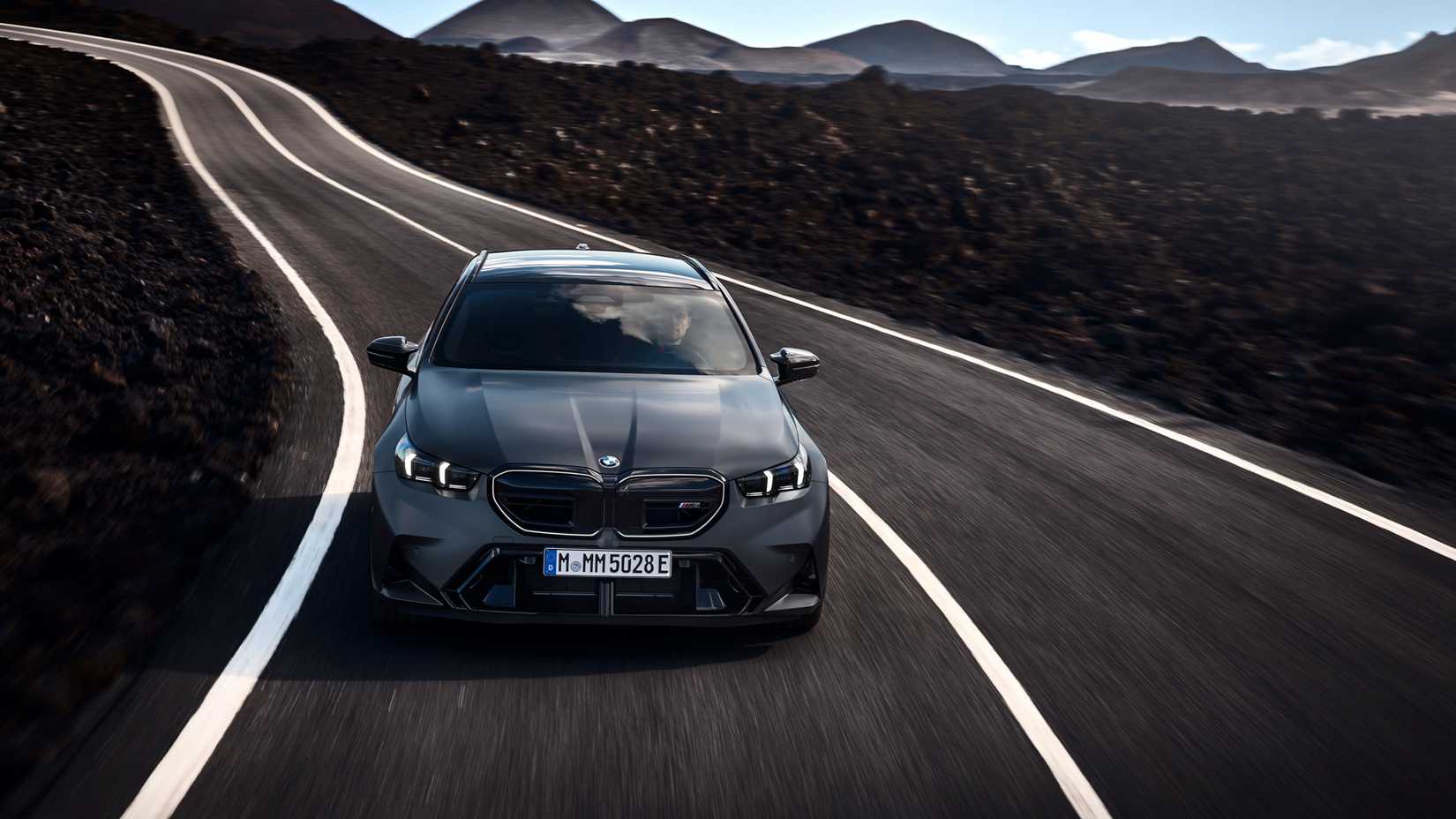 2025 BMW M5 Touring em cinza dirigindo em estrada de montanha