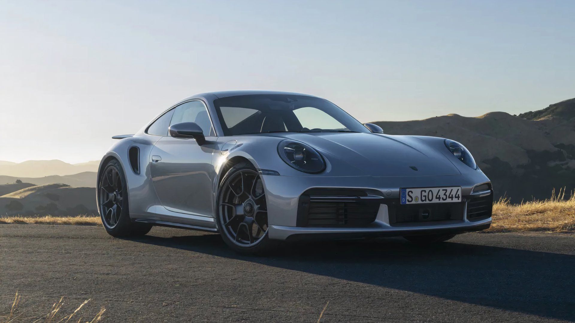 Porsche 911 Turbo 2024 em prata posando em frente a uma cadeia de montanhas