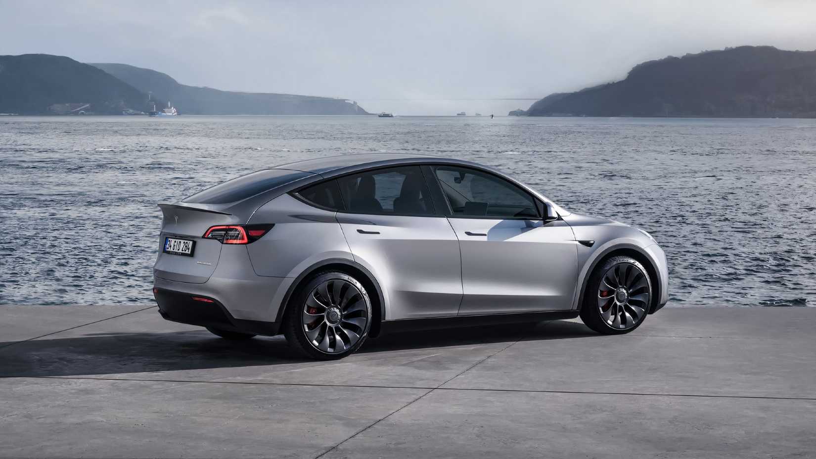 Um Tesla Model Y cinza está estacionado perto da água.