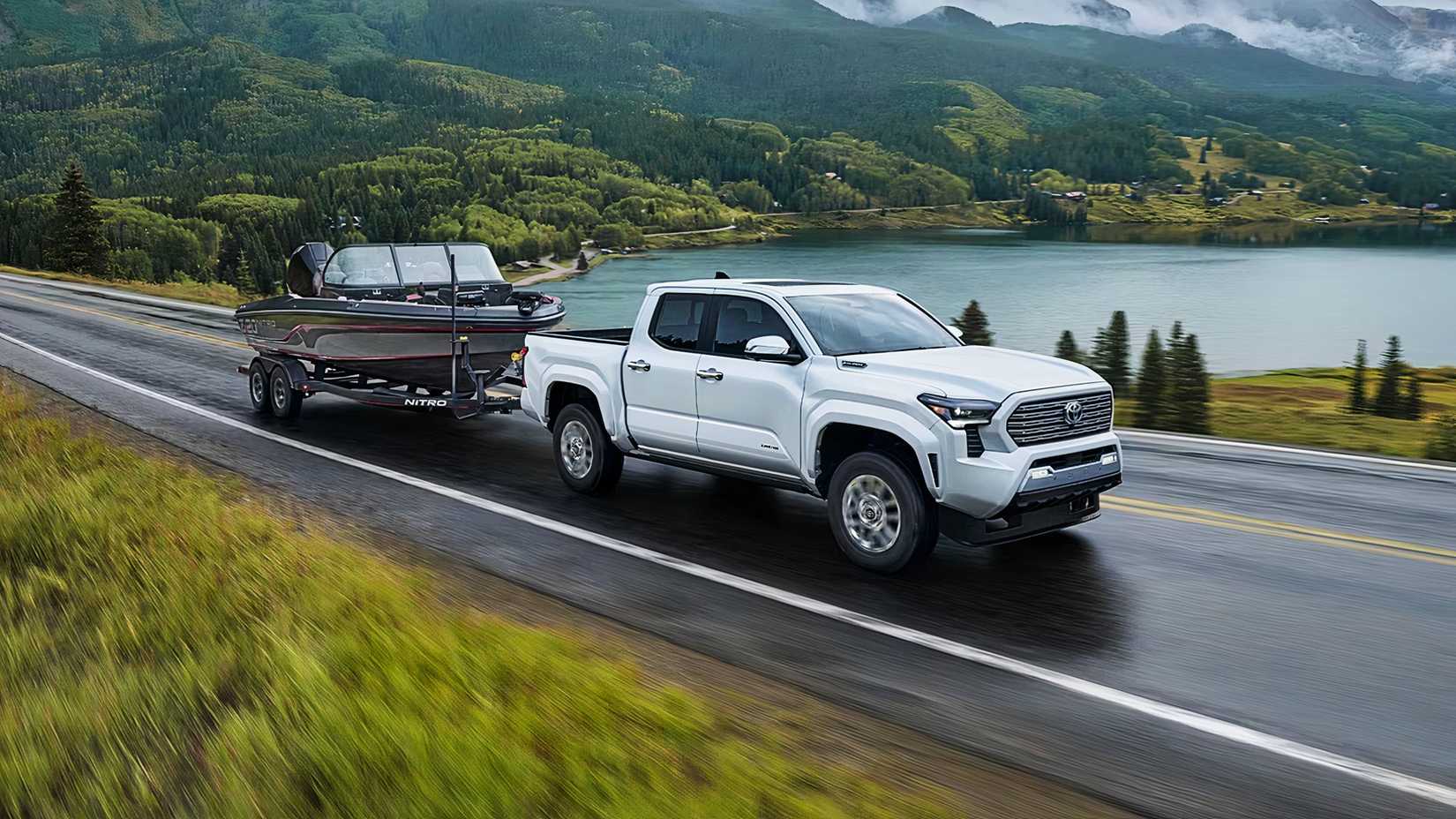 A white Toyota Tacoma Hybrid is towing a boat.