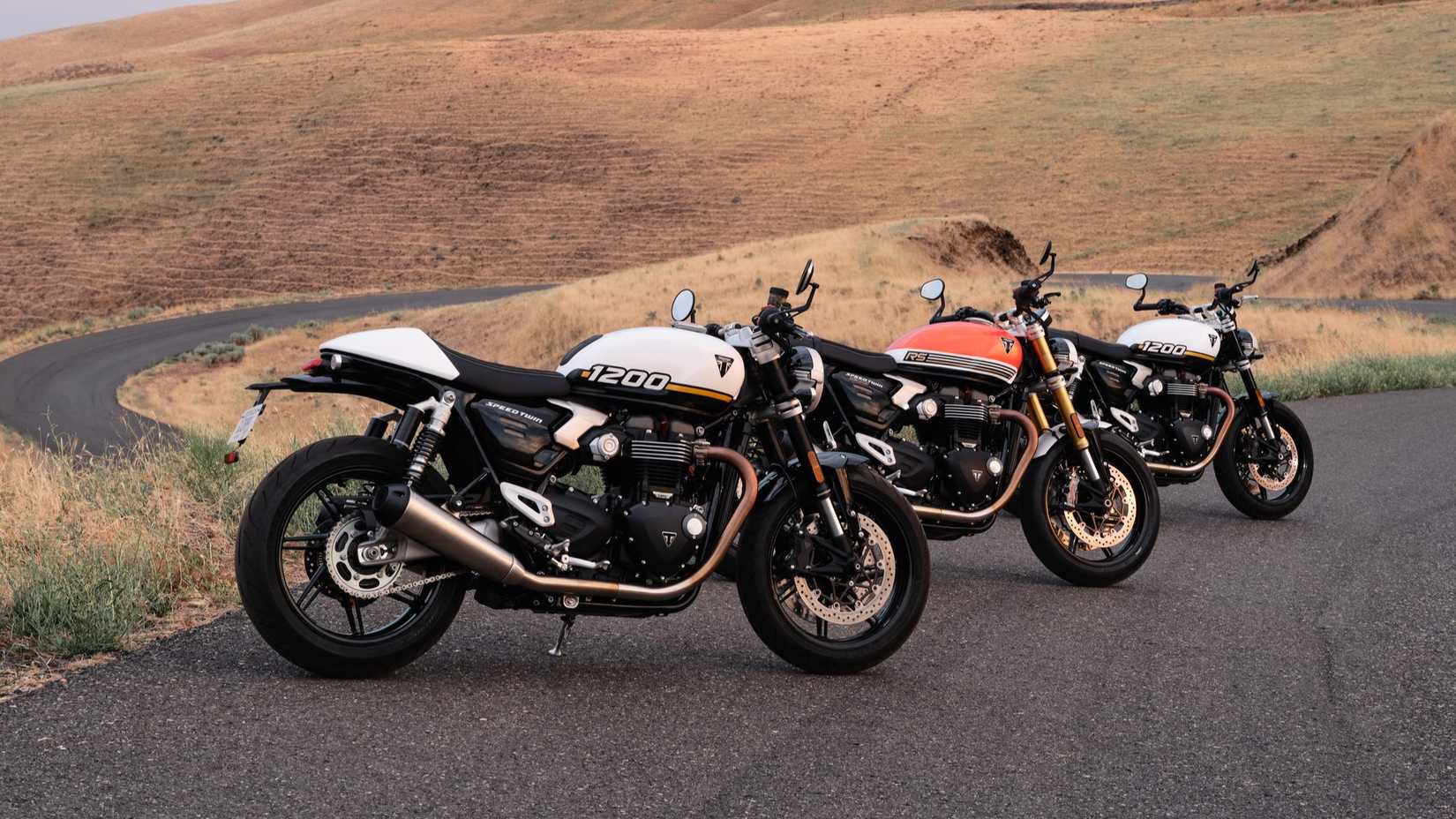 The 2025 Triumph Speed ​​Twin 1200 lineup parked at the edge of a parking lot, overlooking a bend in the road below
