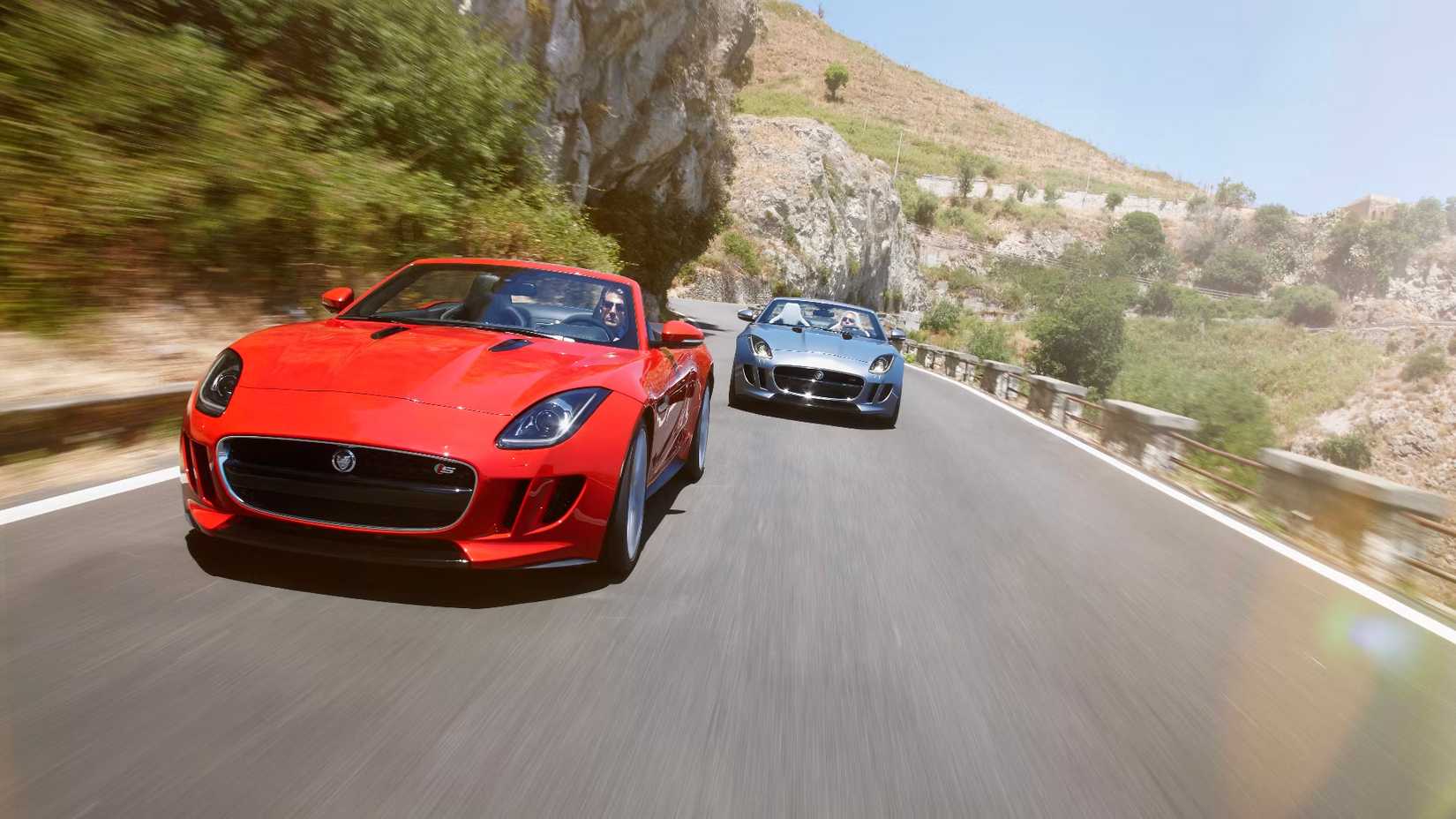 Uma foto de dois carros esportivos Jaguar F-Type dirigindo em uma estrada com muito vento