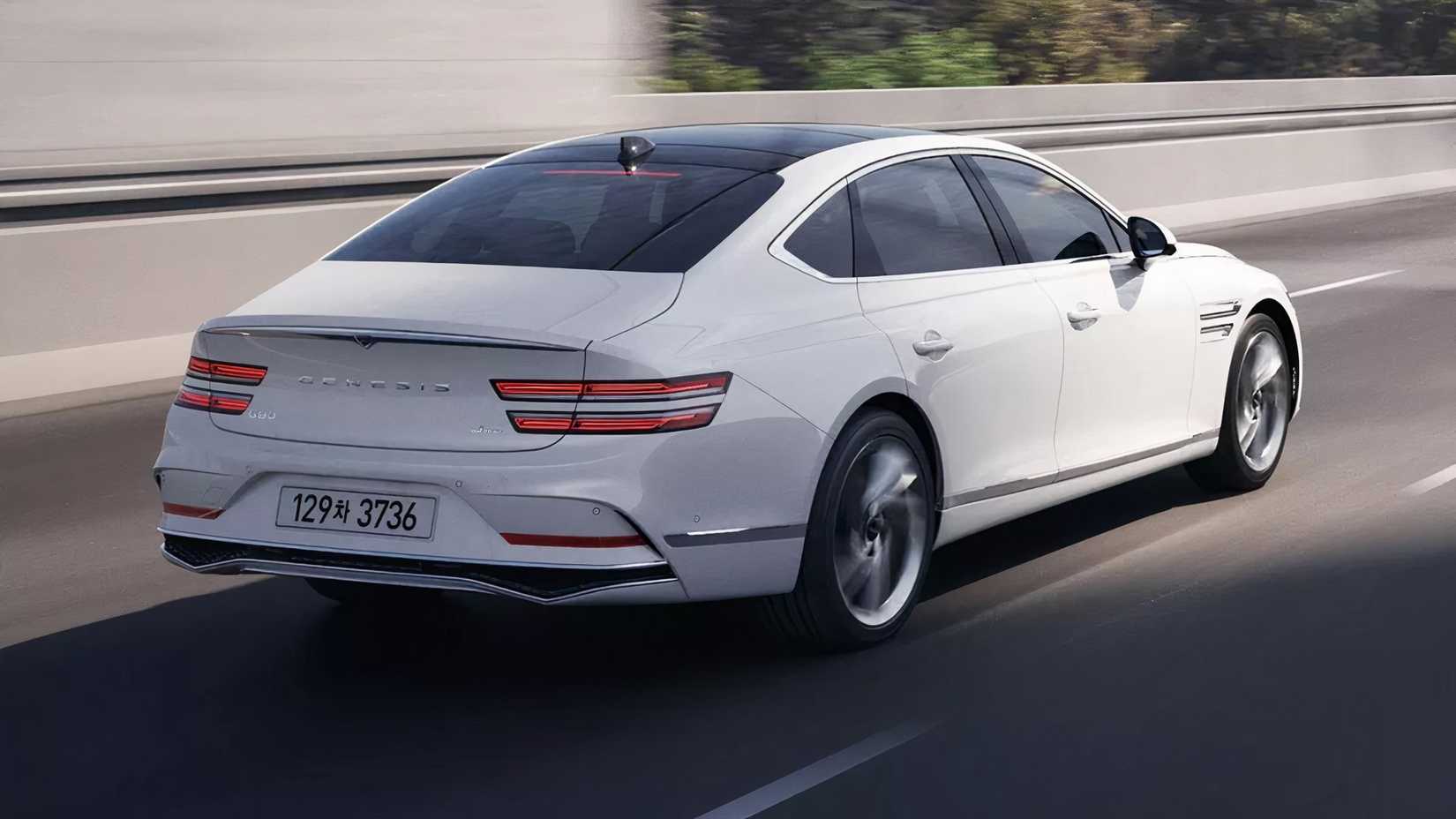 Rear shot of a white Genesis G80 cruising down highway at speed