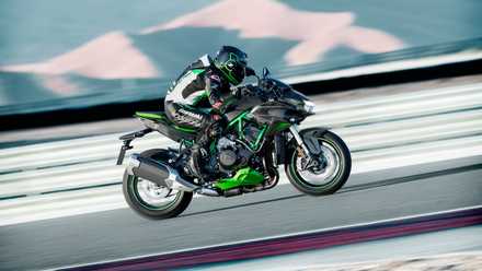 Foto de ação de um piloto agachado sobre uma Kawasaki Z H2 com uma grade de proteção ao fundo