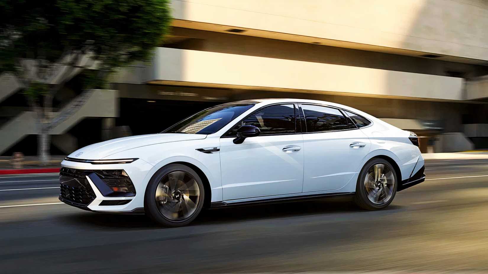 A white Hyundai Sonata Hybrid midsize hybrid sedan is driving on the road. 