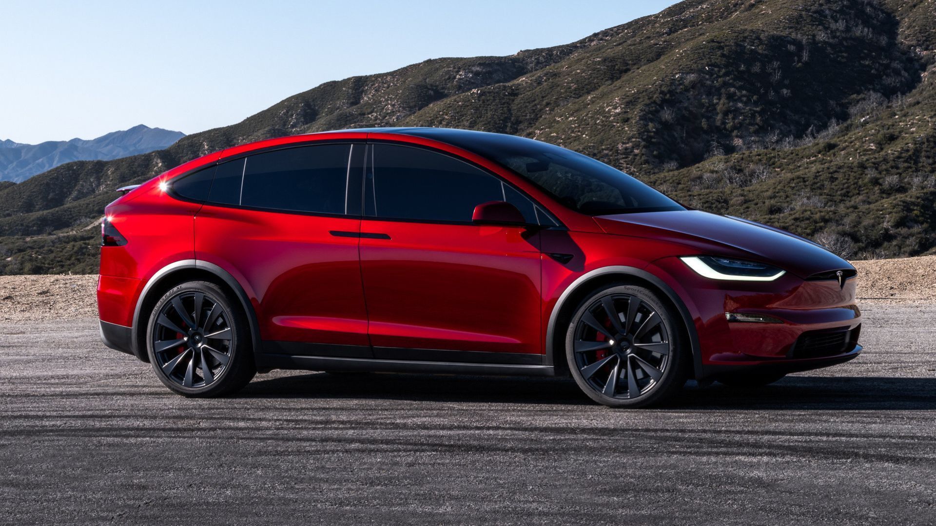 2024 Tesla Model X em vermelho posando off-road em frente a colinas
