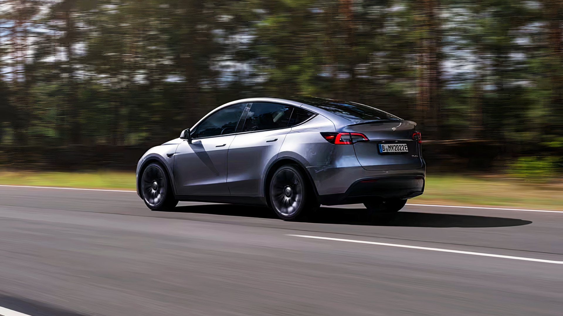 Um pequeno SUV elétrico Tesla Model Y 2024 cinza está circulando na estrada.