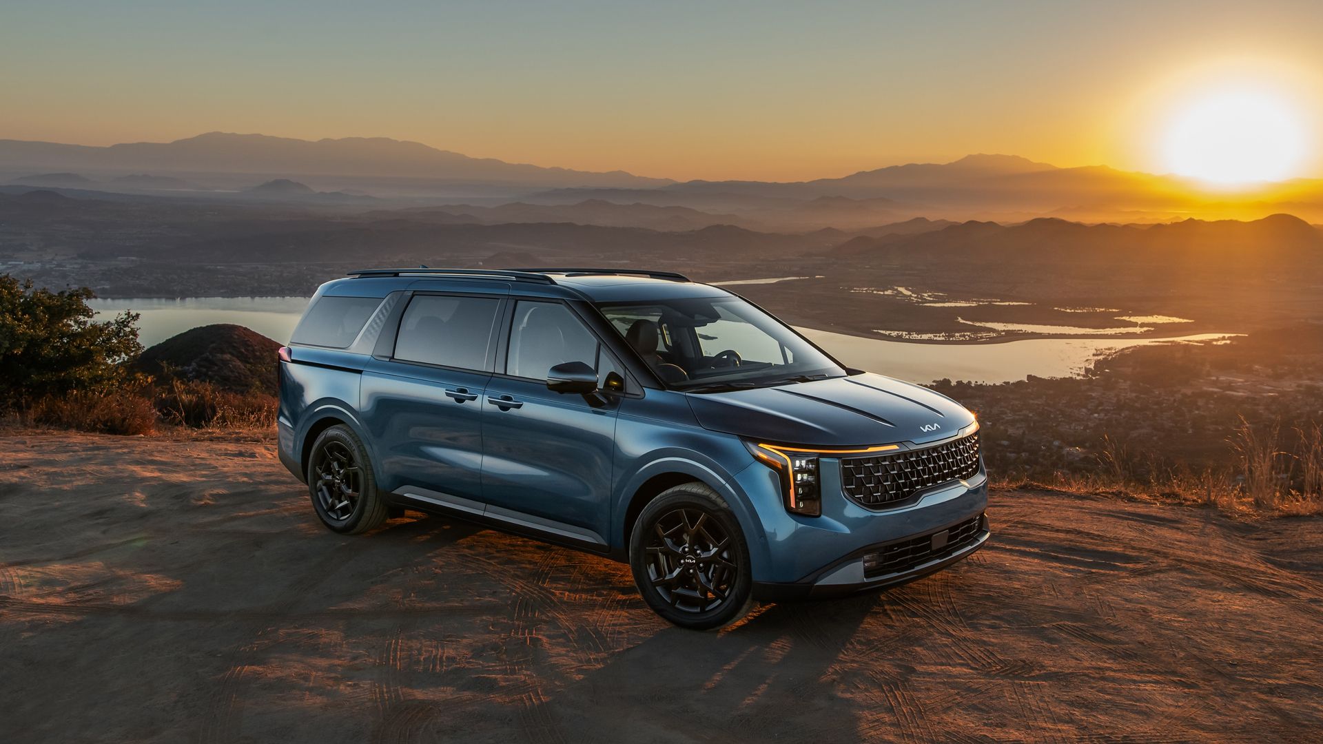 2025 Kia Carnival in blue parked off-road in front of mountain range