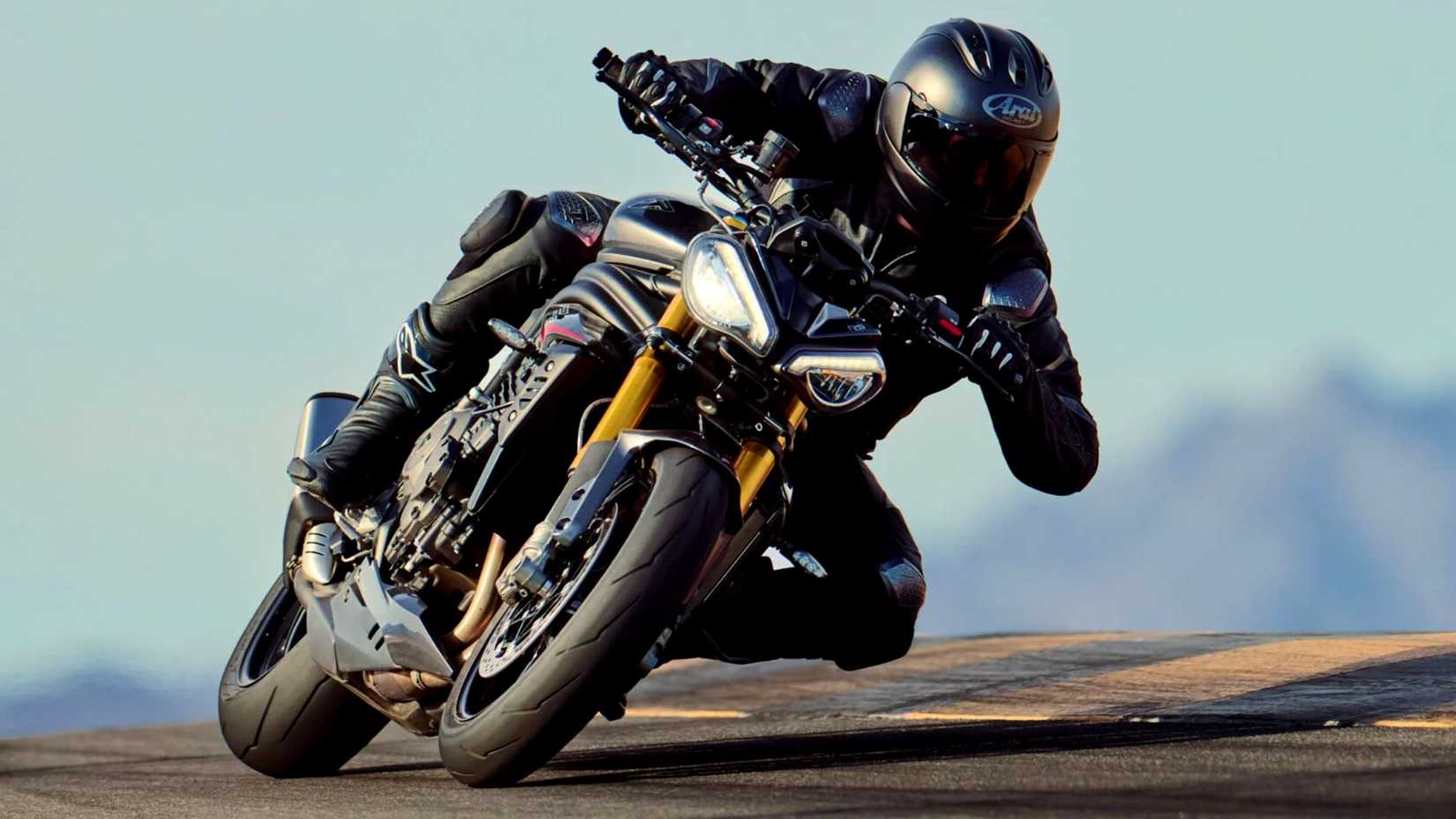 2025 Triumph Speed Triple 1200 RS Fazendo curvas em uma pista de corrida com montanhas ao fundo