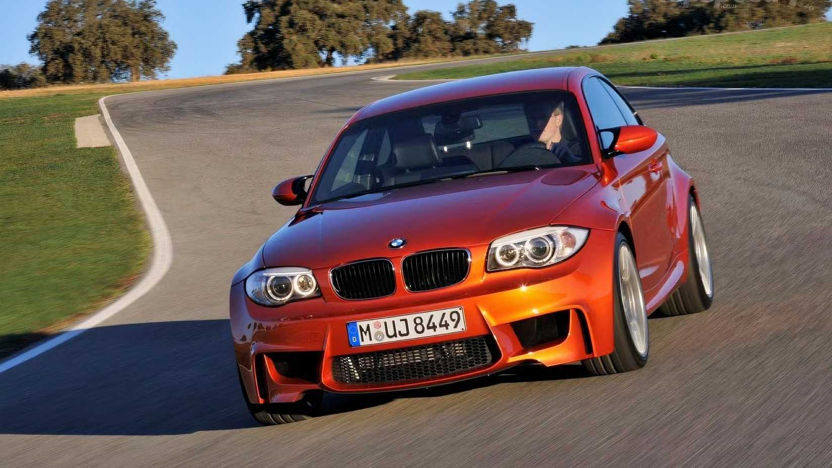 2011 BMW 1 Series M in orange driving on a racetrack