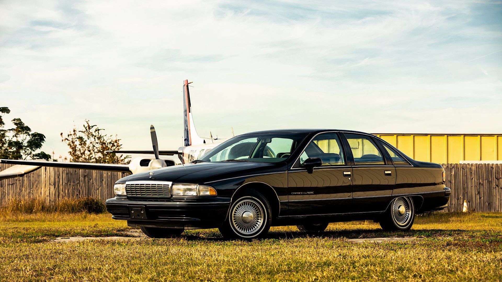 1991 Chevrolet Caprice in black parked on grass in front of airplane