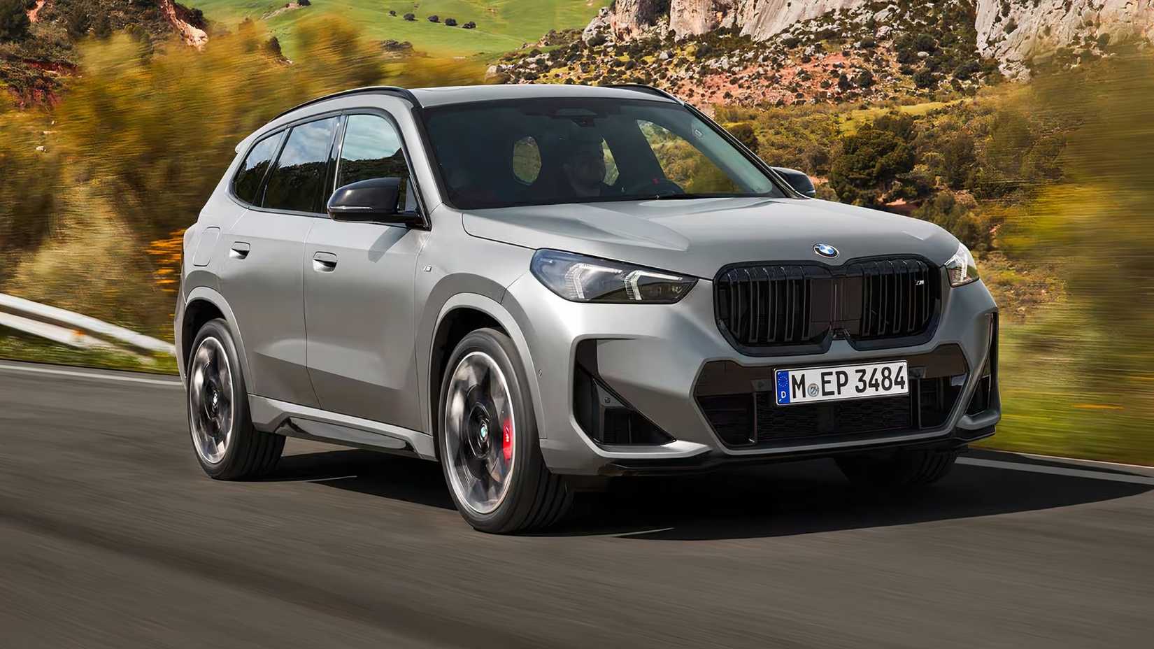 Foto frontal de ação 3/4 do BMW X1 M35i 2025 em prata dirigindo em uma estrada secundária