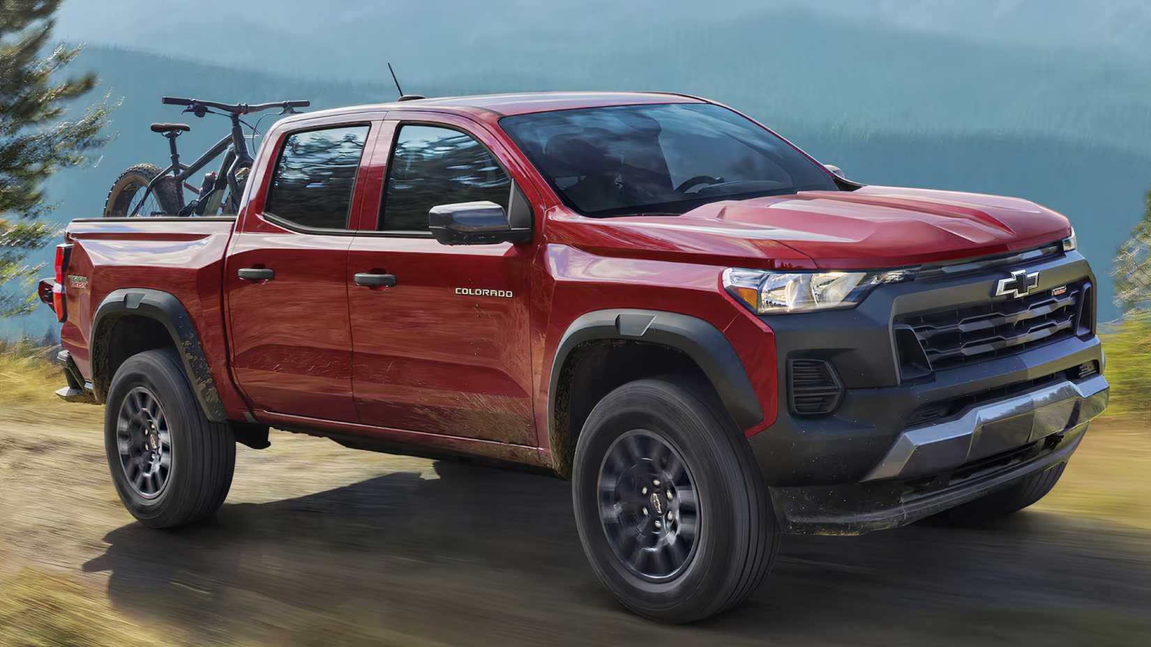 2025 Chevrolet Colorado in red driving on dirt road with bike in bed