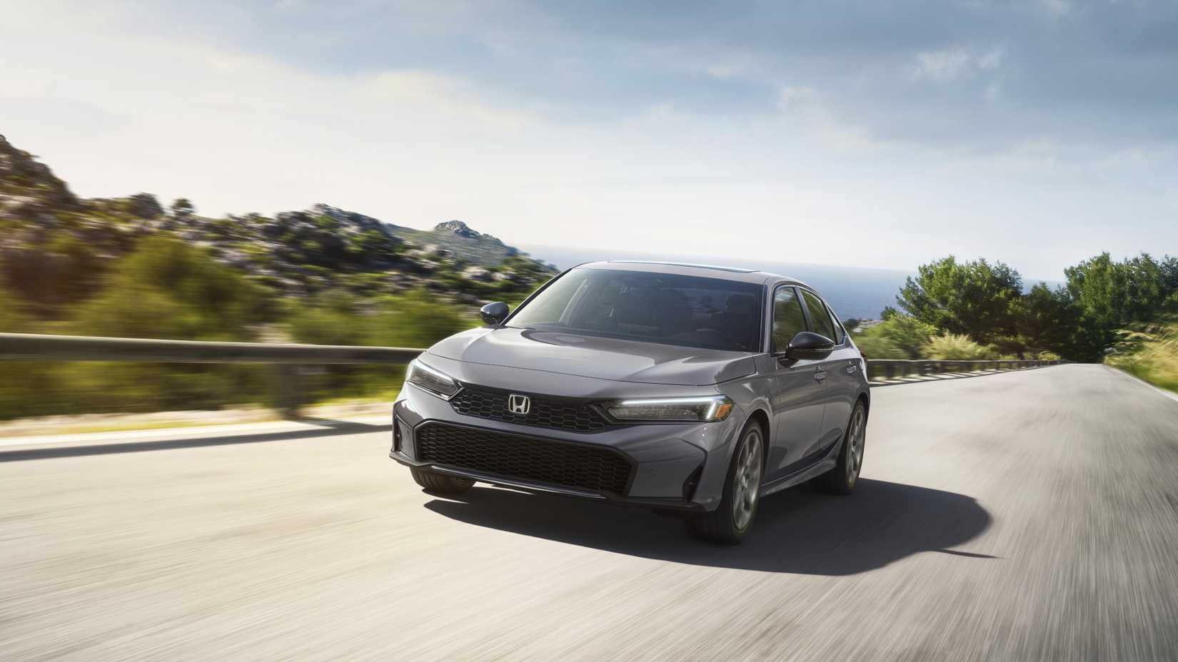 2025 Honda Civic Hatchback Sport Touring Hybrid Front Exterior Driving Down A Road