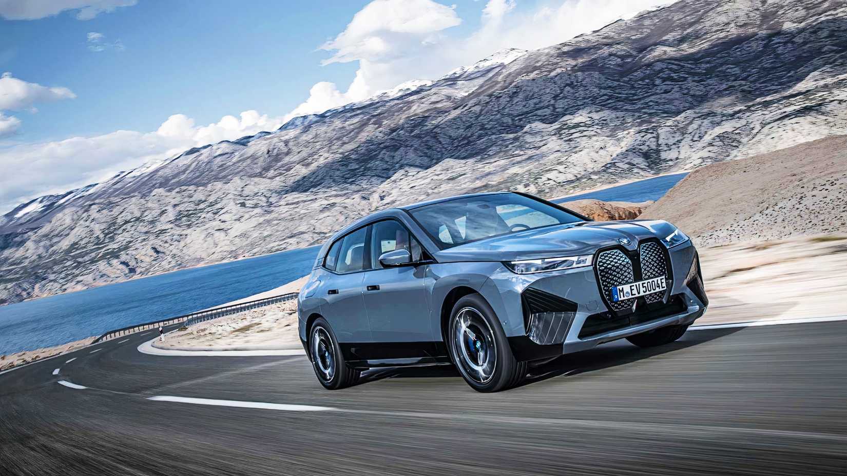 A blue 2022 BMW iX midsize electric SUV is driving on the road. 