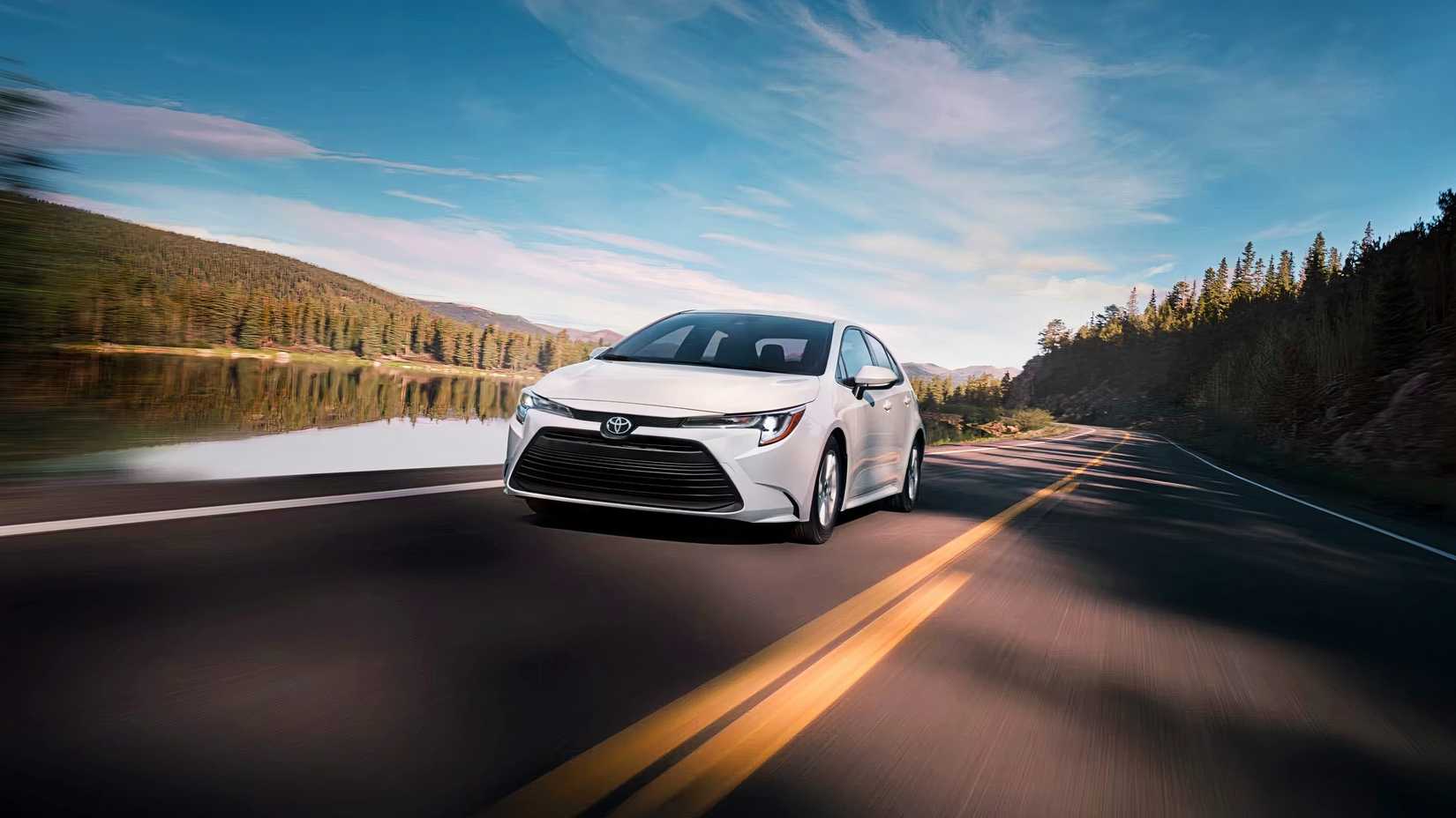 A white 2025 Toyota Corolla Hybrid sedan is driving on the road. 