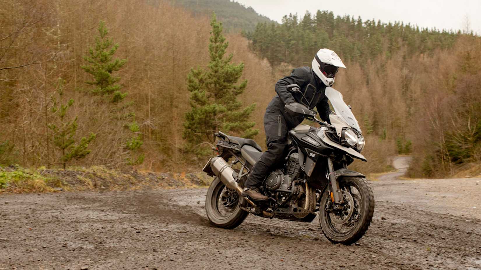 Foto lateral de uma Triumph Tiger 1200 Desert Edition em trilha de terra