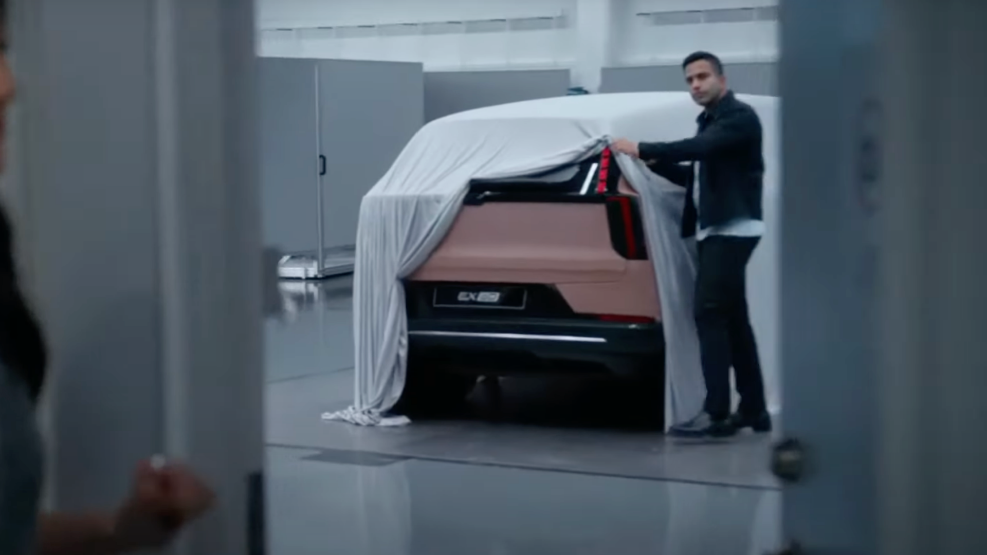 A man holding a sheet covering the Volvo EX60 electric crossover