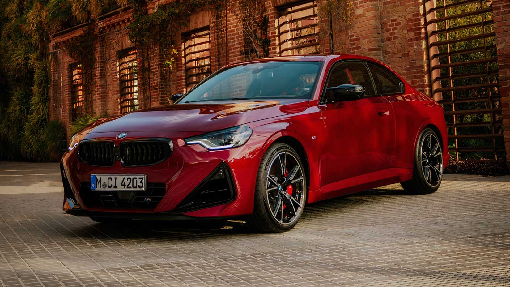 Foto frontal 3/4 de um BMW M240i xDrive 2025 vermelho estacionado em frente à casa