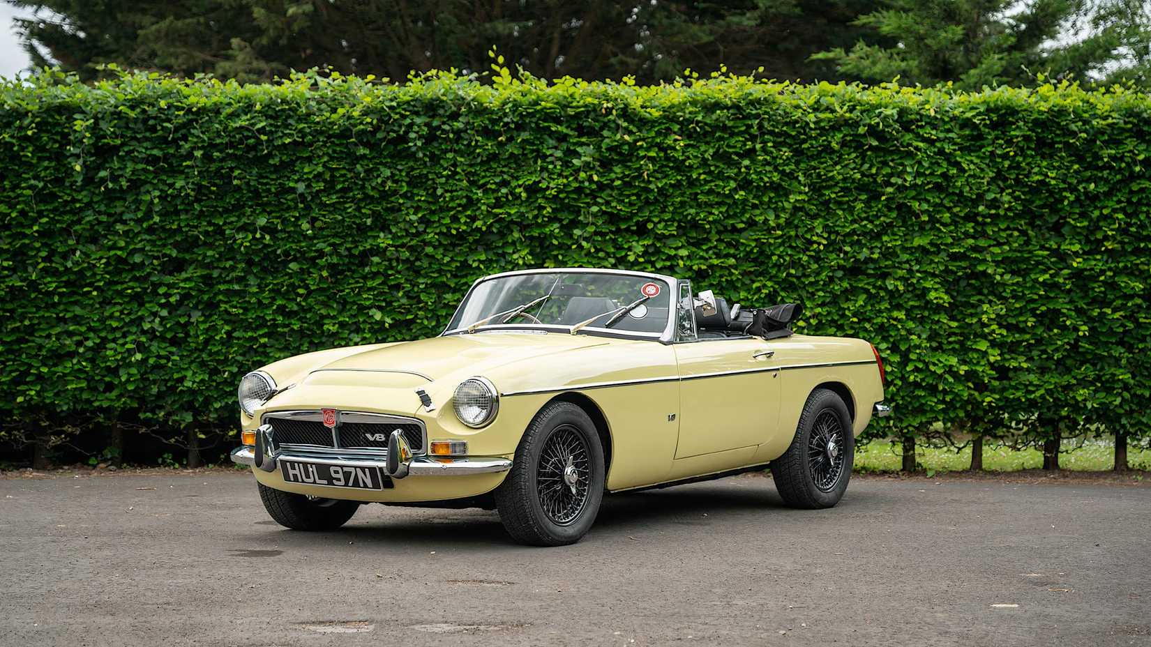 1975 MG B Roadster V8 in yellow parked in front of hedge