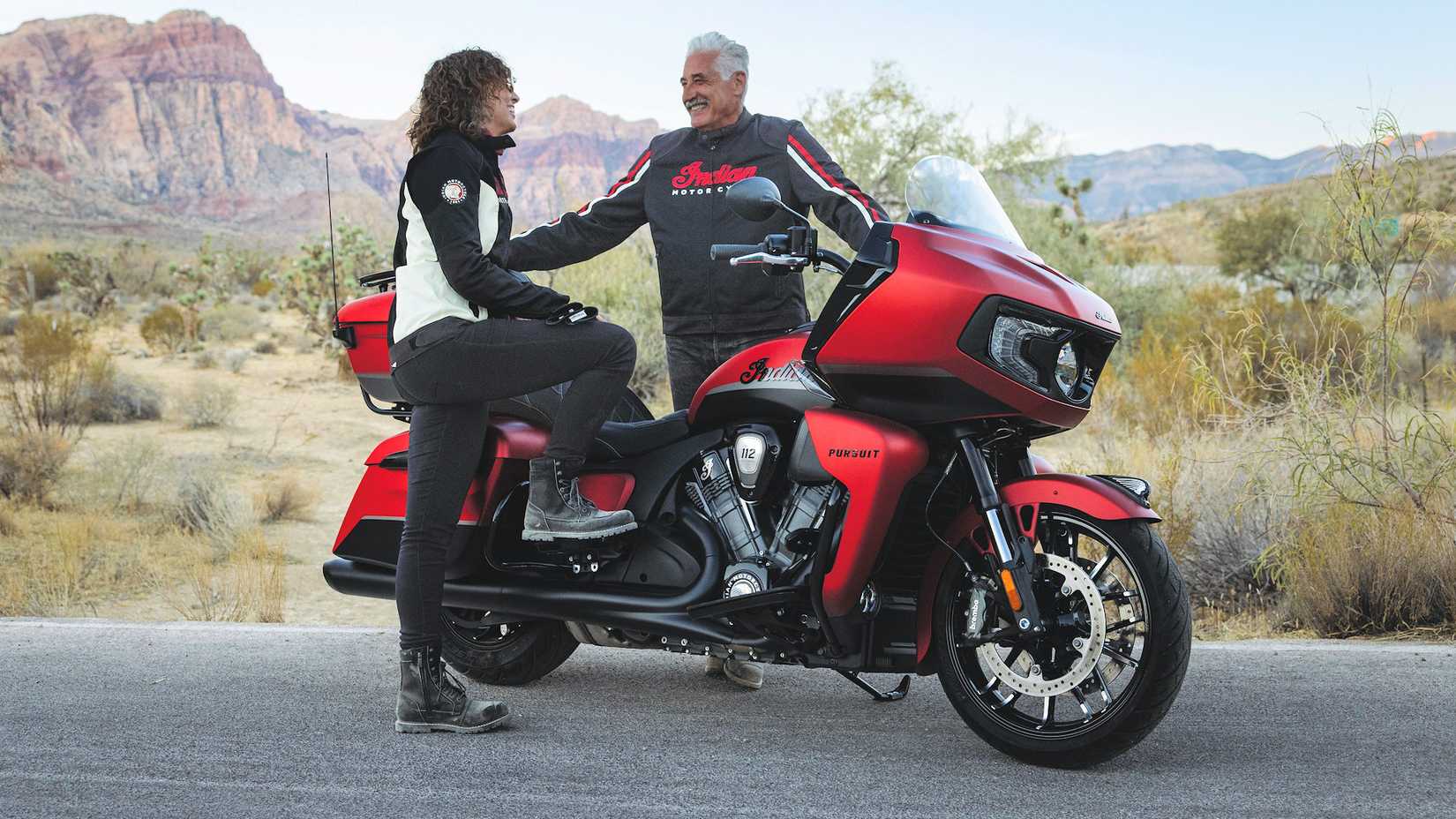 Rider and passenger standing next to a 2025 Indian Pursuit Dark Horse