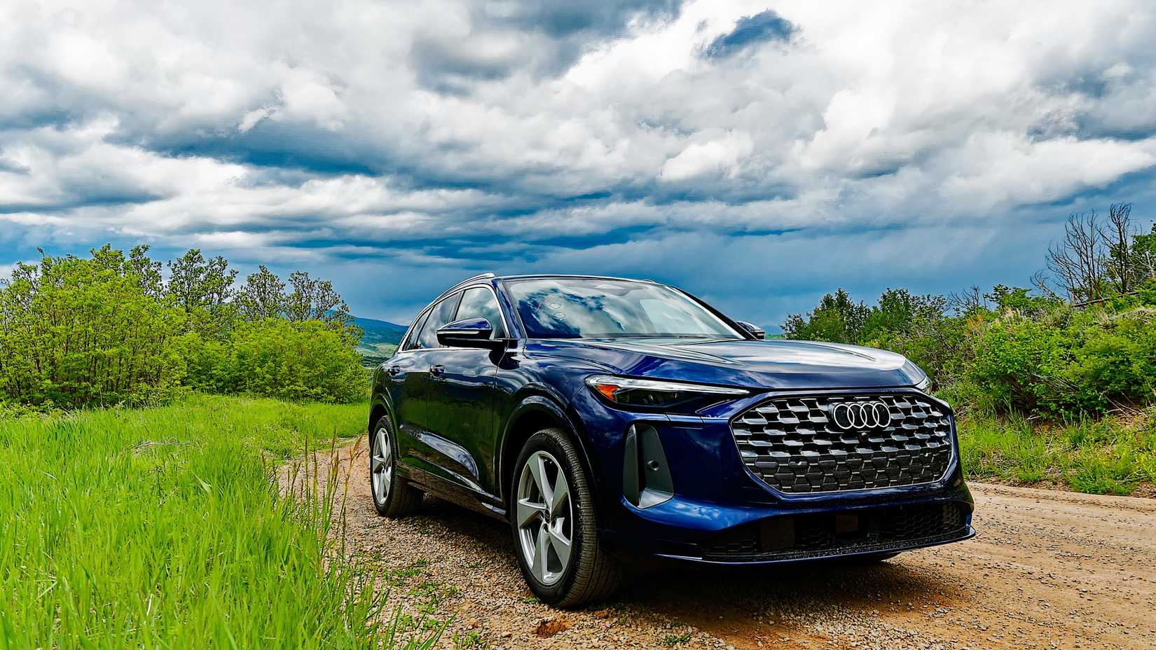 Foto frontal 3/4 de um Audi Q5 2025 azul estacionado em estrada de terra