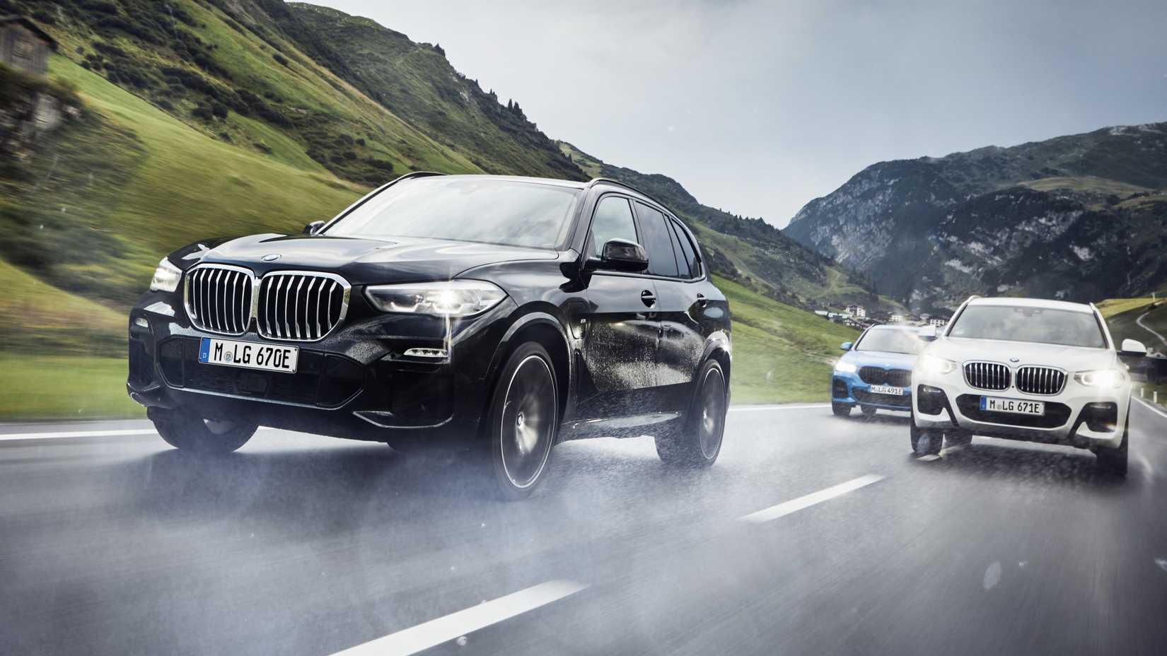 A dynamic front-quarter tracking shot of three BMW X3 xDrive30e models driving through a damp mountain pass