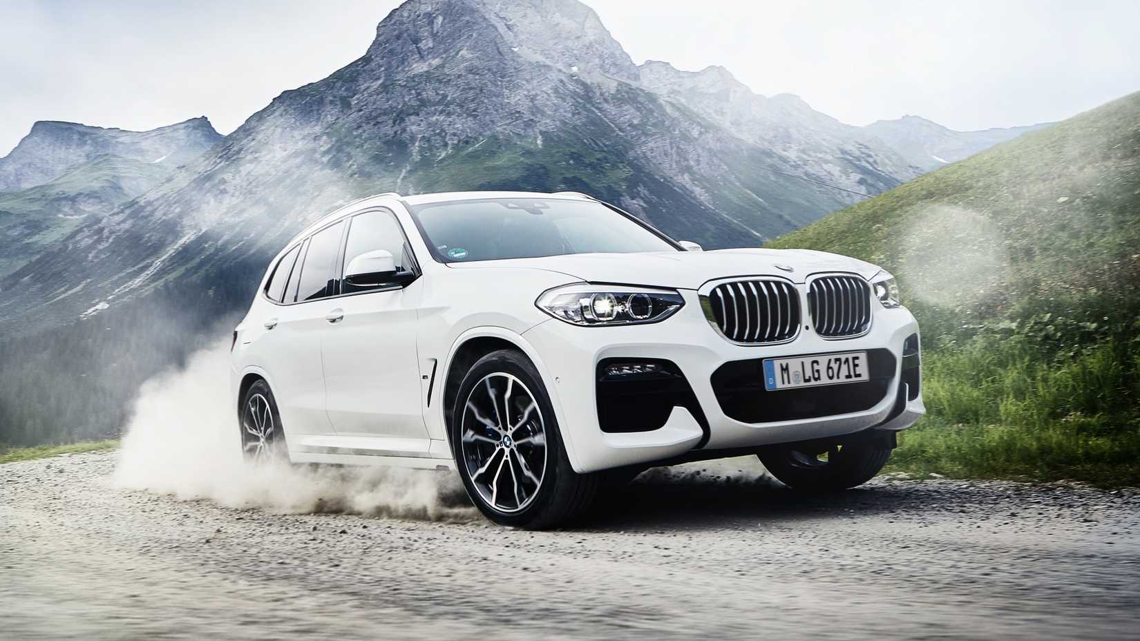 A dynamic front-quarter action shot of a white 2022 BMW X3 xDrive30e driving through gravel