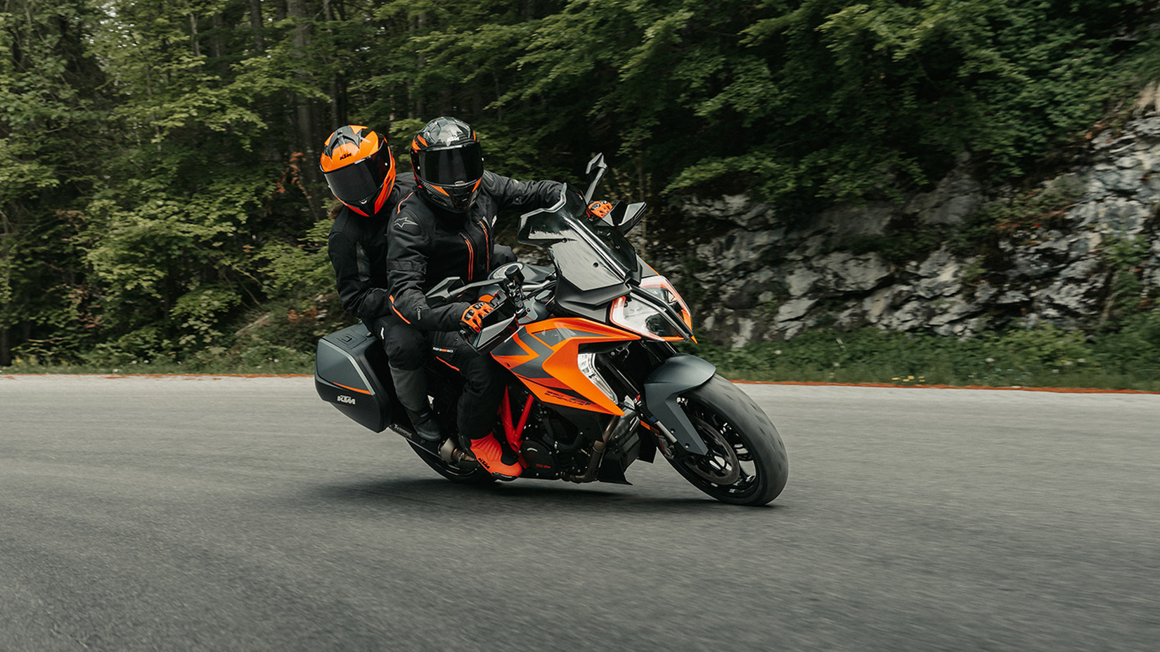 KTM 1290 Super Duke GT fazendo curvas em uma estrada de montanha com piloto e passageiro